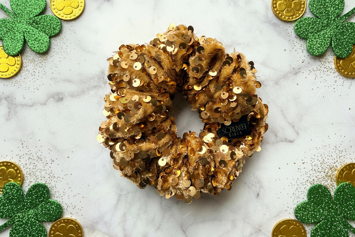 Gold sequin scrunchie on a marble surface with shamrocks and gold coins.