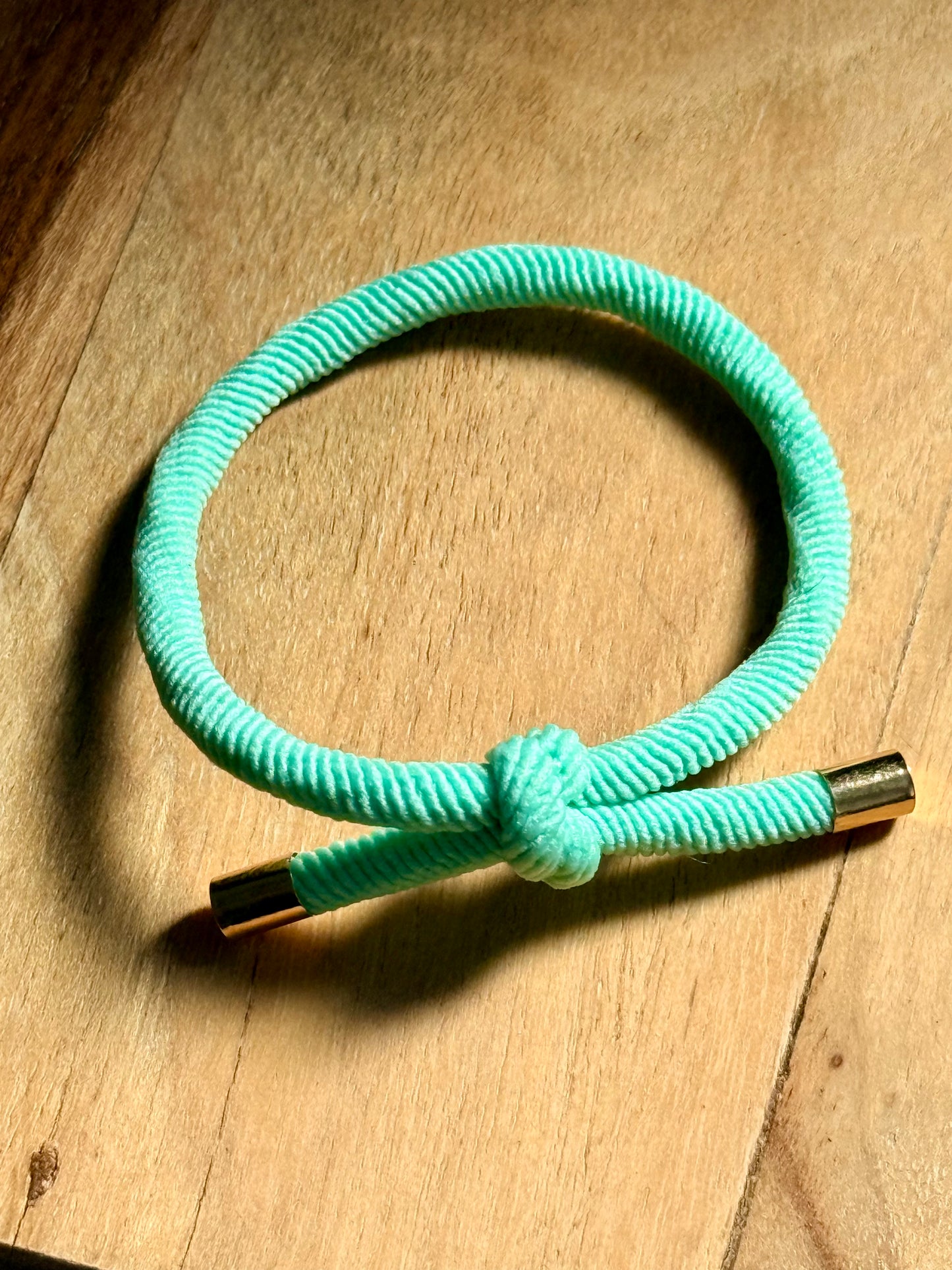 Turquoise braided bracelet with a gold clasp on a wooden surface