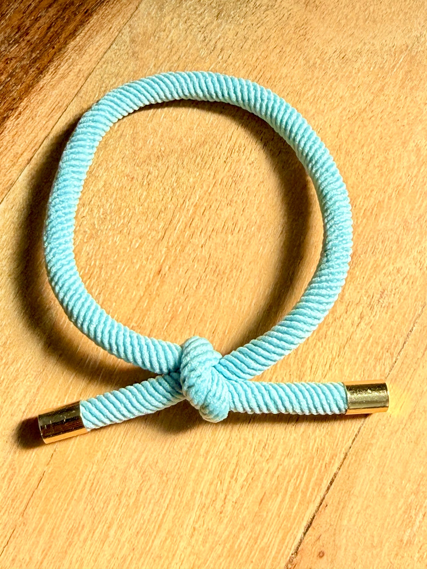 Turquoise hair tie with gold ends on a wooden surface