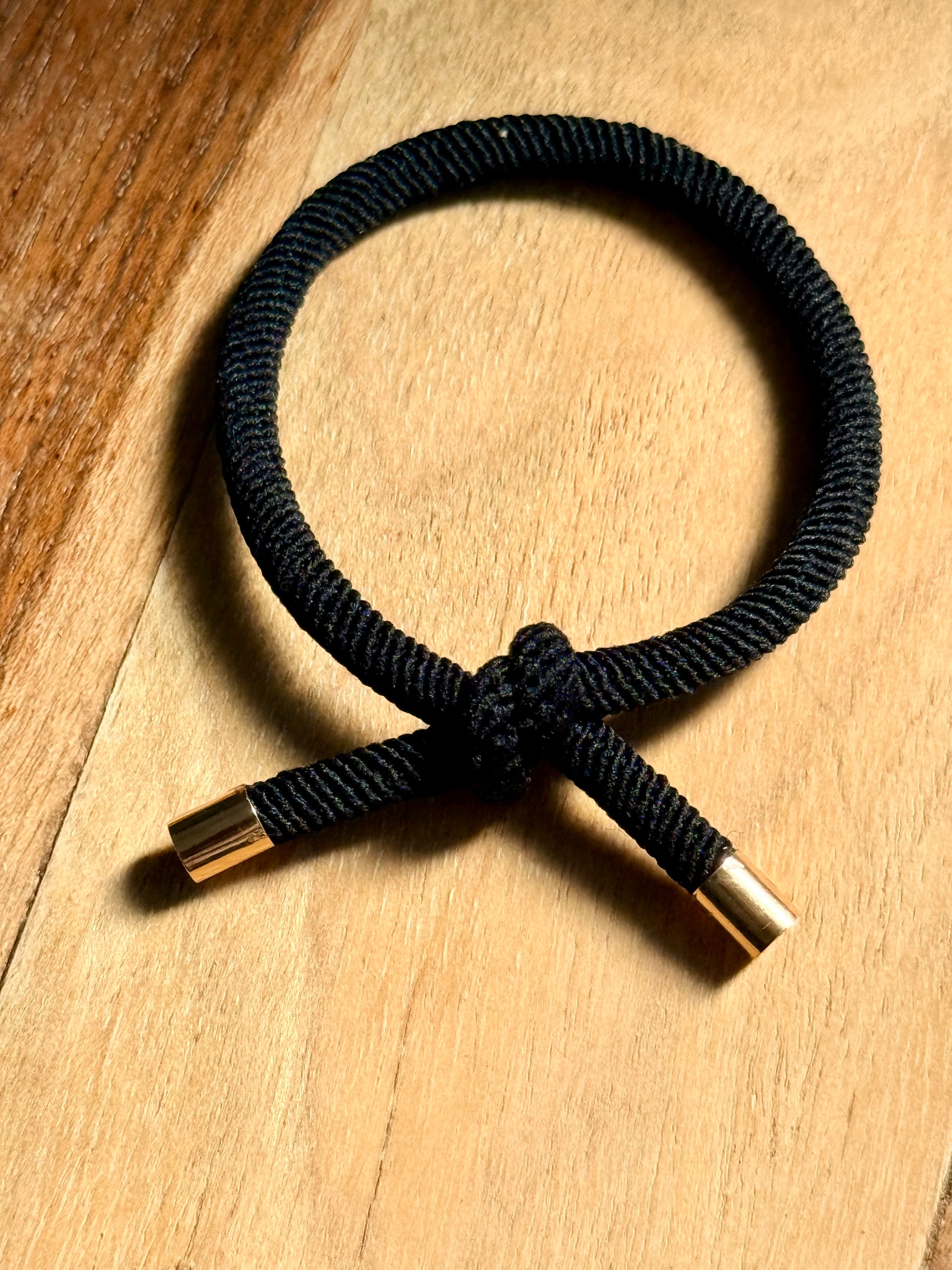 Black hair tie with gold ends on a wooden surface