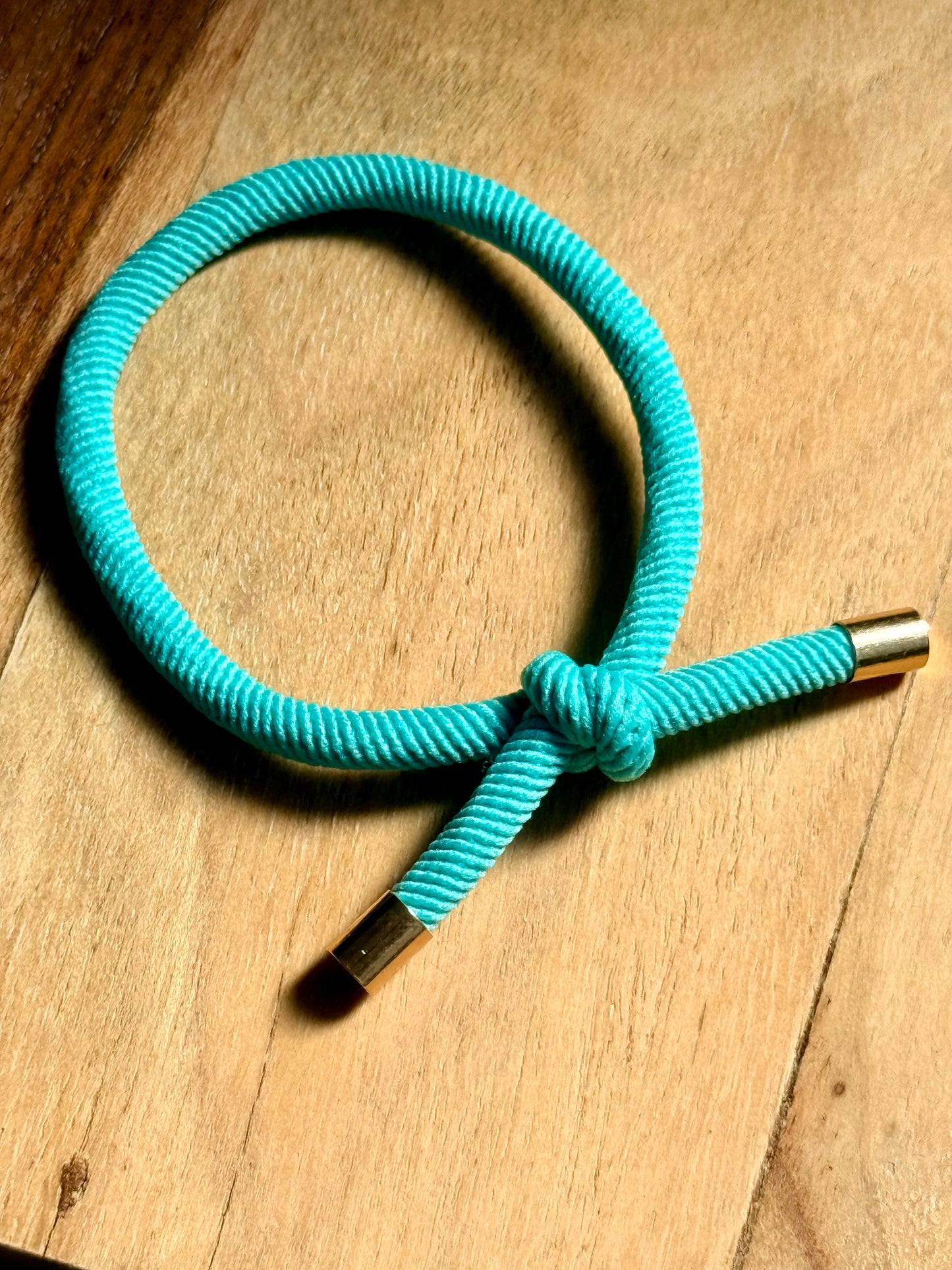 Turquoise rope with gold ends on a wooden surface