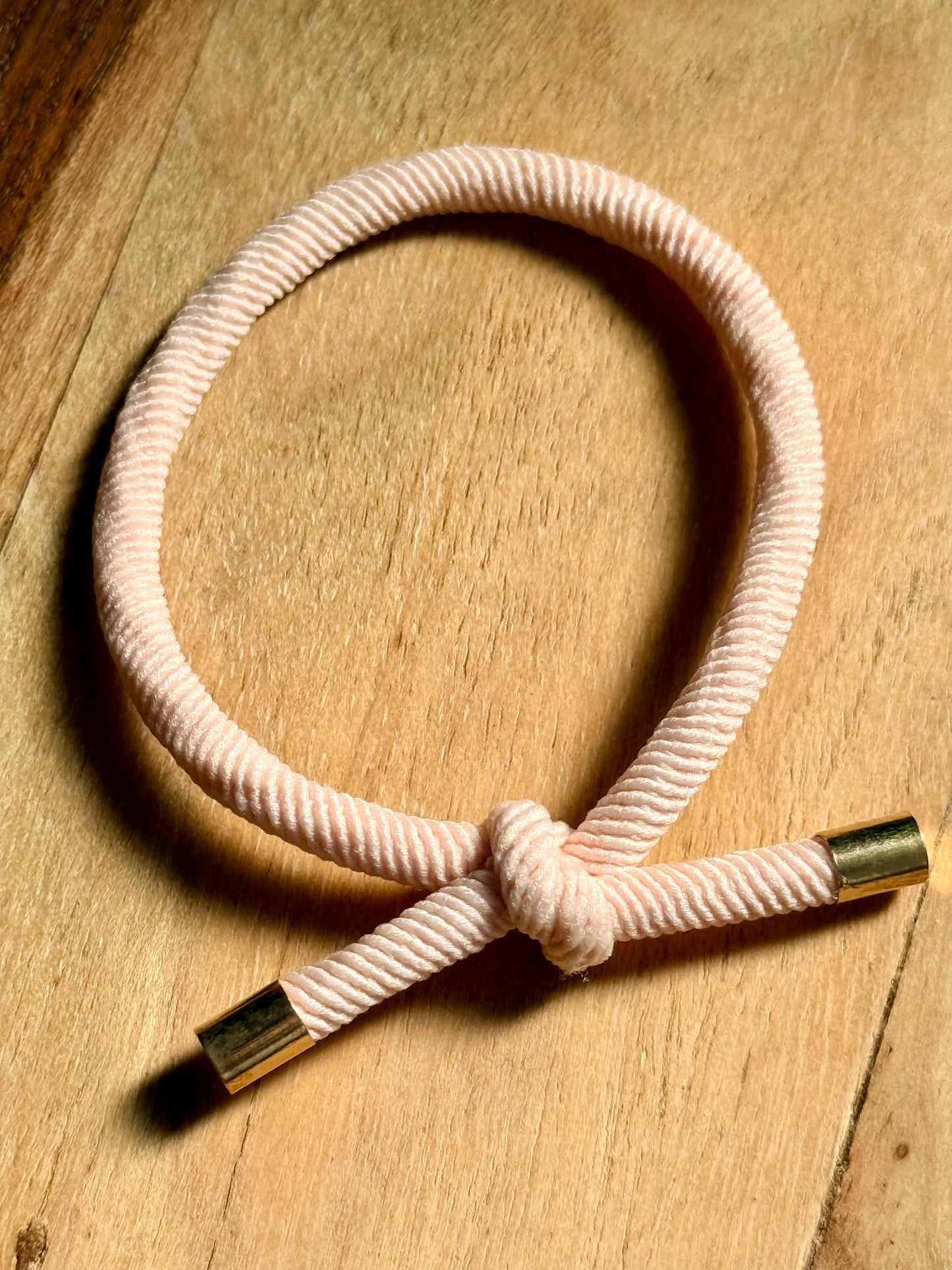 a pastel pink knotted hair tie with metal ends that can also be worn as a bracelet