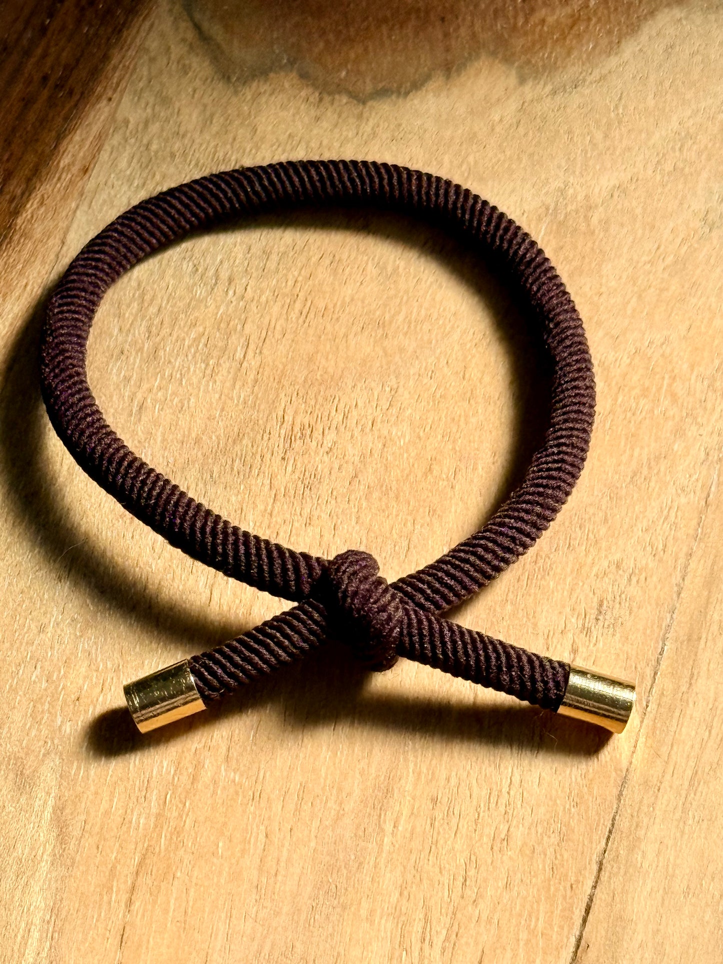 Brown corded bracelet with gold clasp on a wooden surface