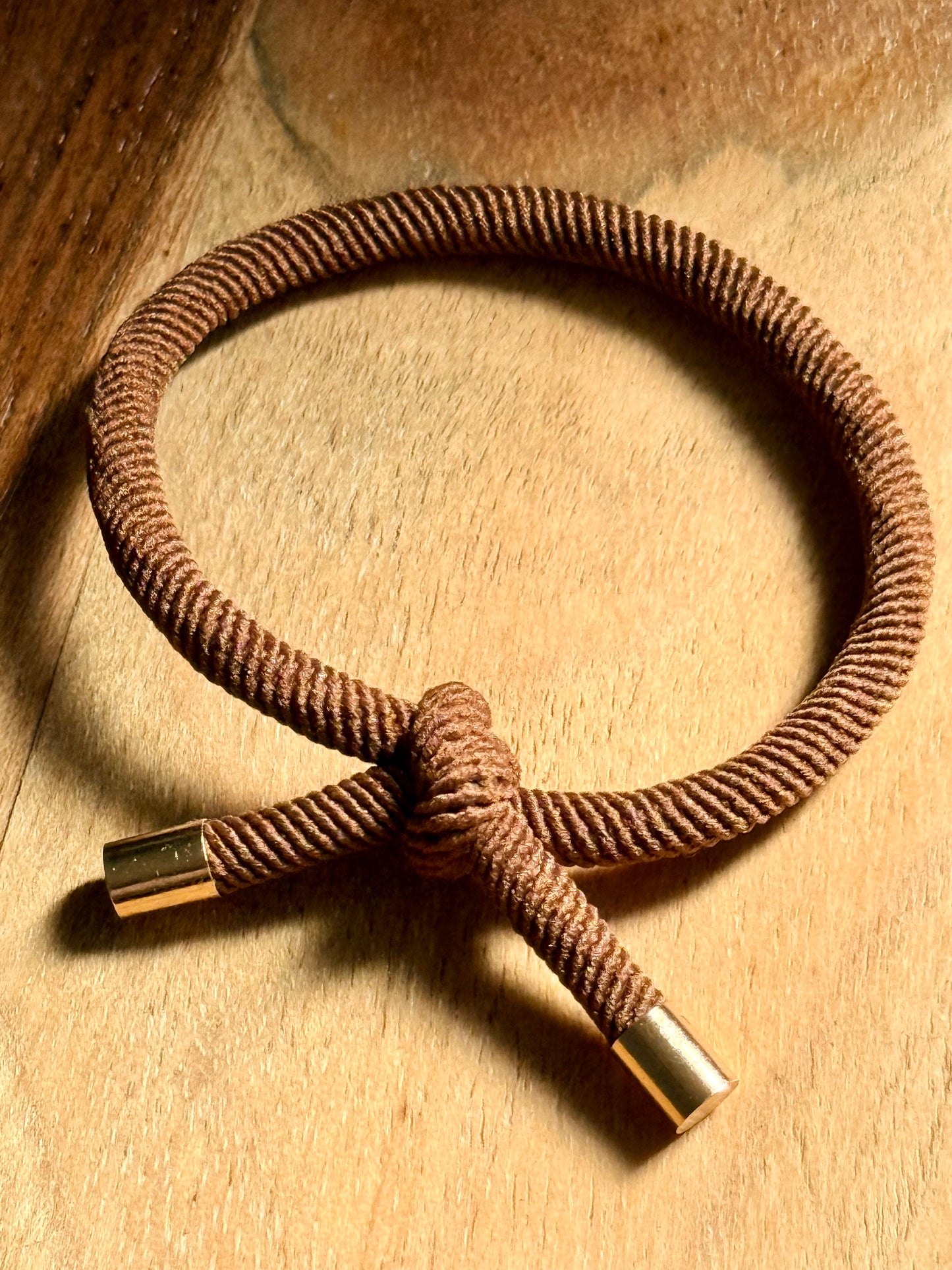 Brown braided bracelet with gold ends on a wooden surface