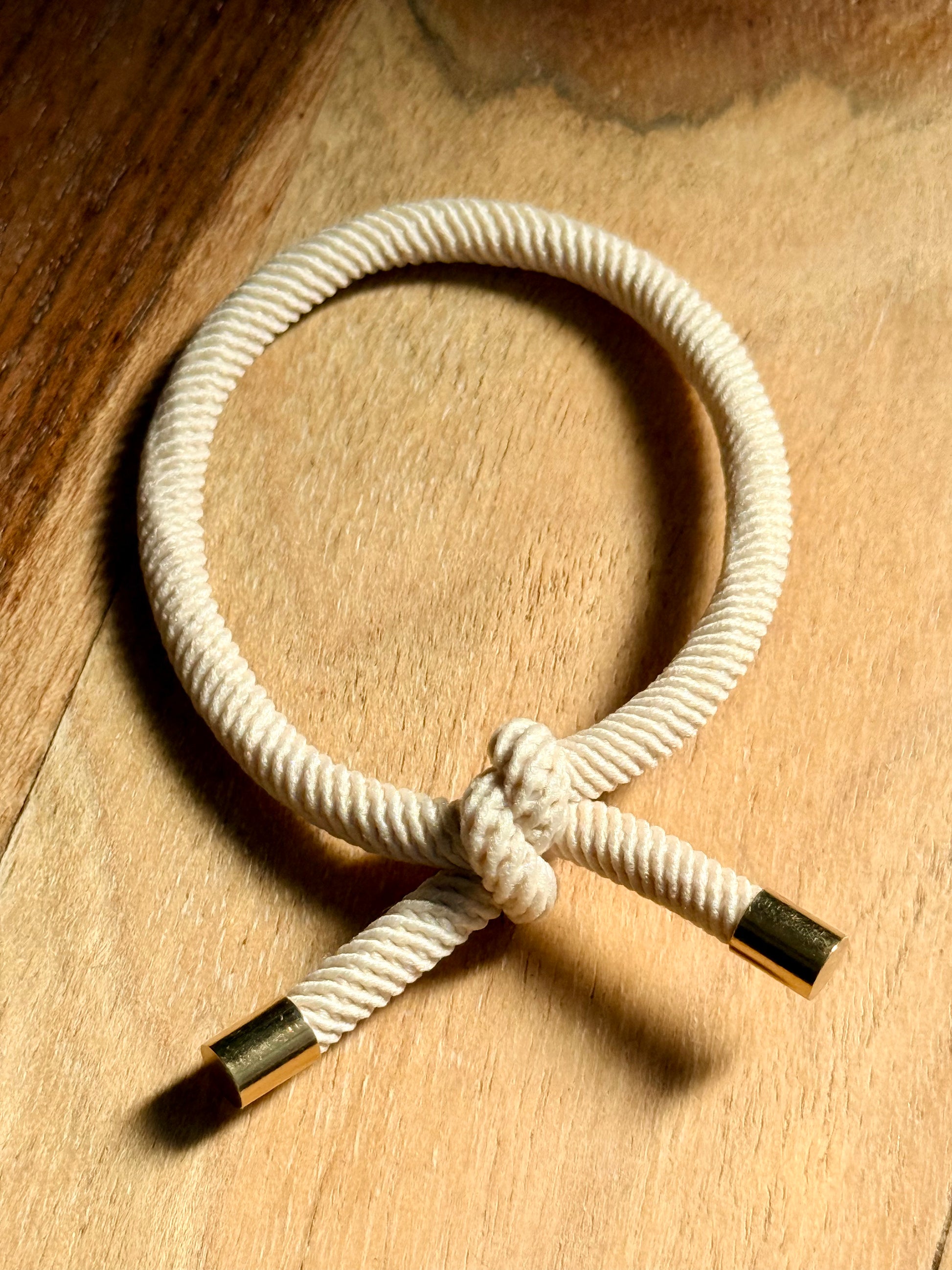 White rope bracelet with gold and black ends on a wooden surface