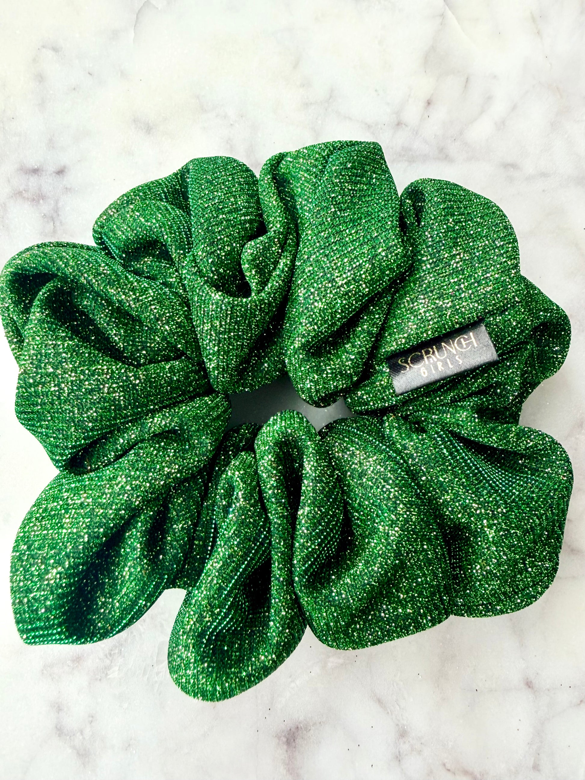 Green glittery scrunchie with brand label on a white marble background
