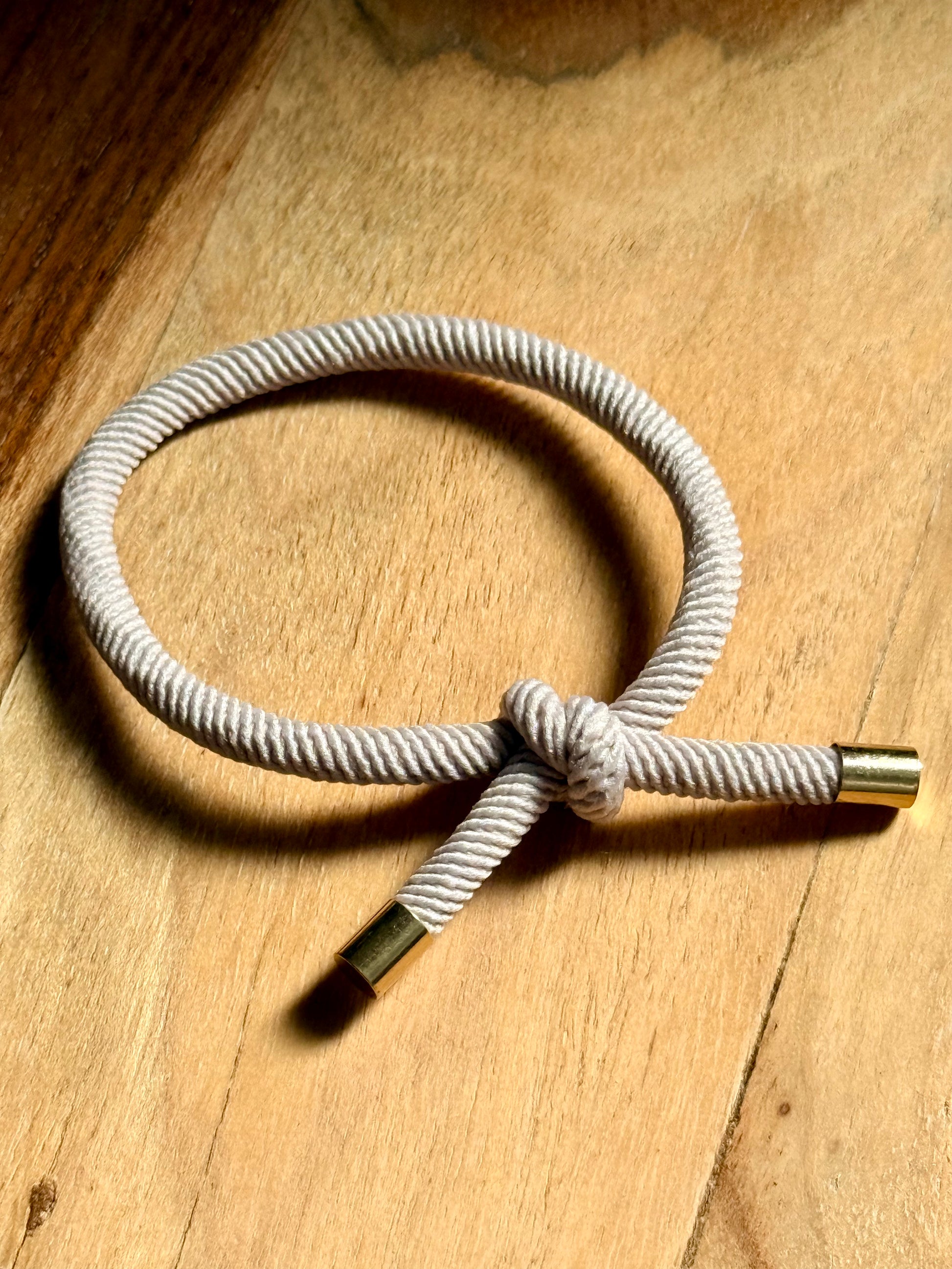 Rope bracelet with gold ends on a wooden surface