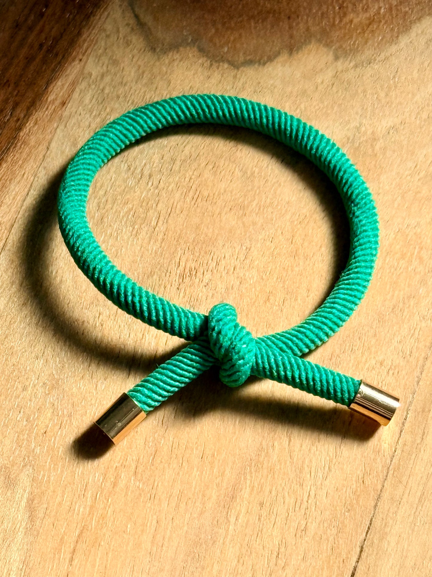 Green braided bracelet with metal ends on a wooden surface