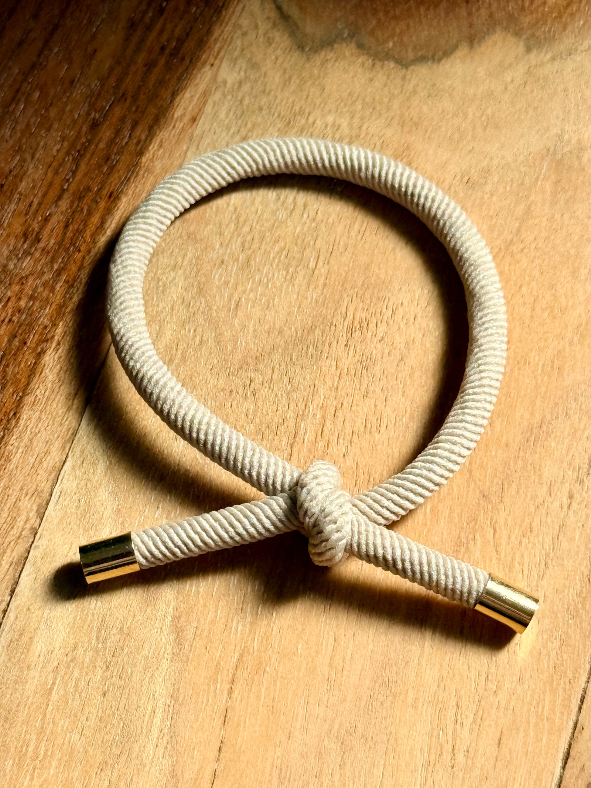 Nautical-style rope bracelet with gold clasp on a wooden surface