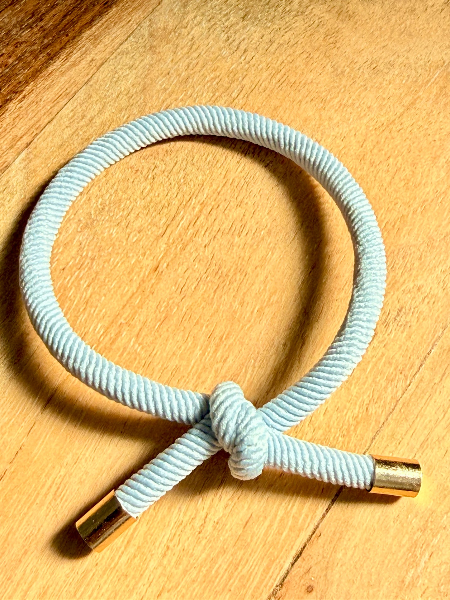 Light blue cord bracelet with gold clasp on a wooden surface