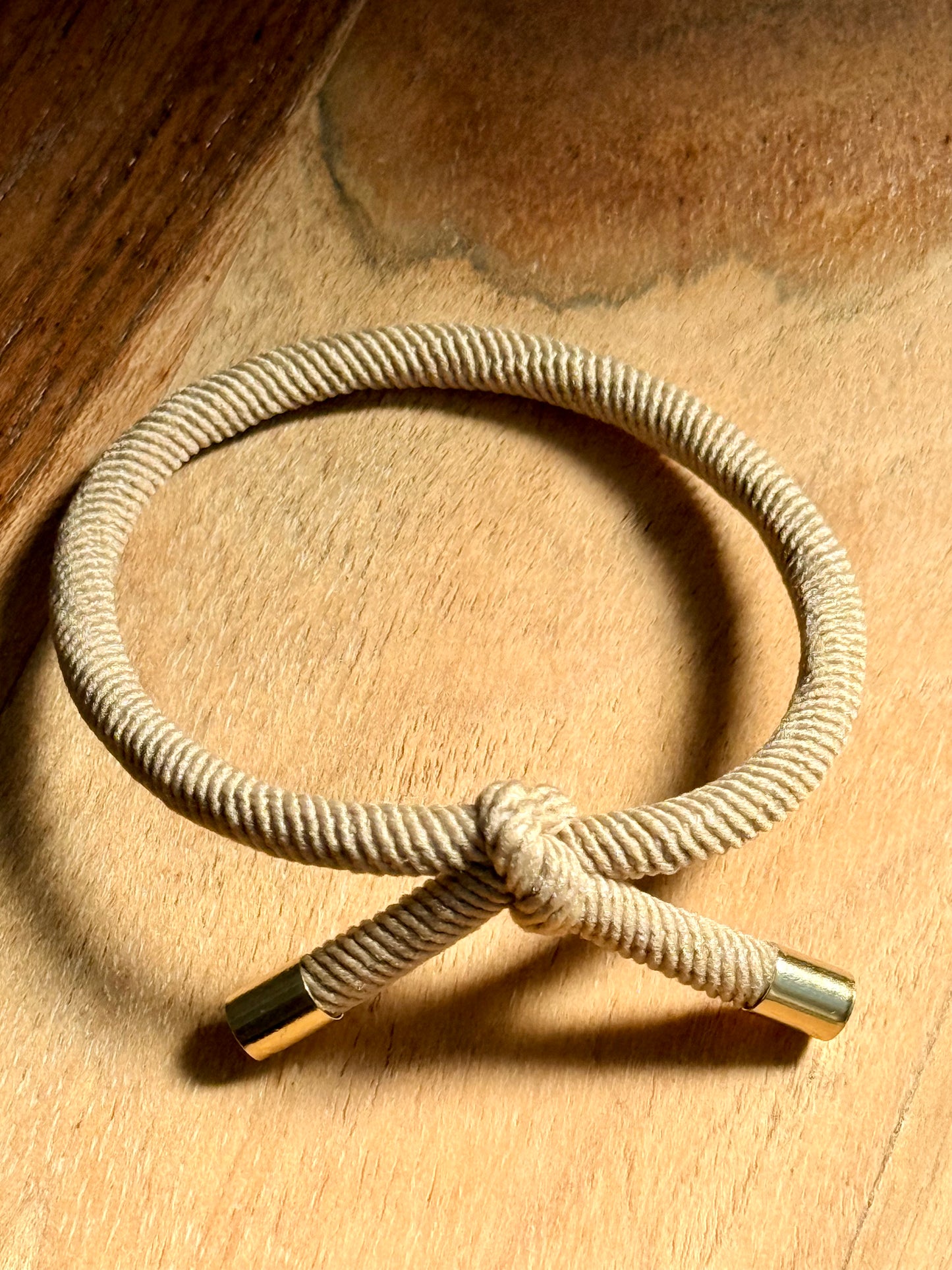 Nautical-style rope bracelet with gold ends on a wooden surface
