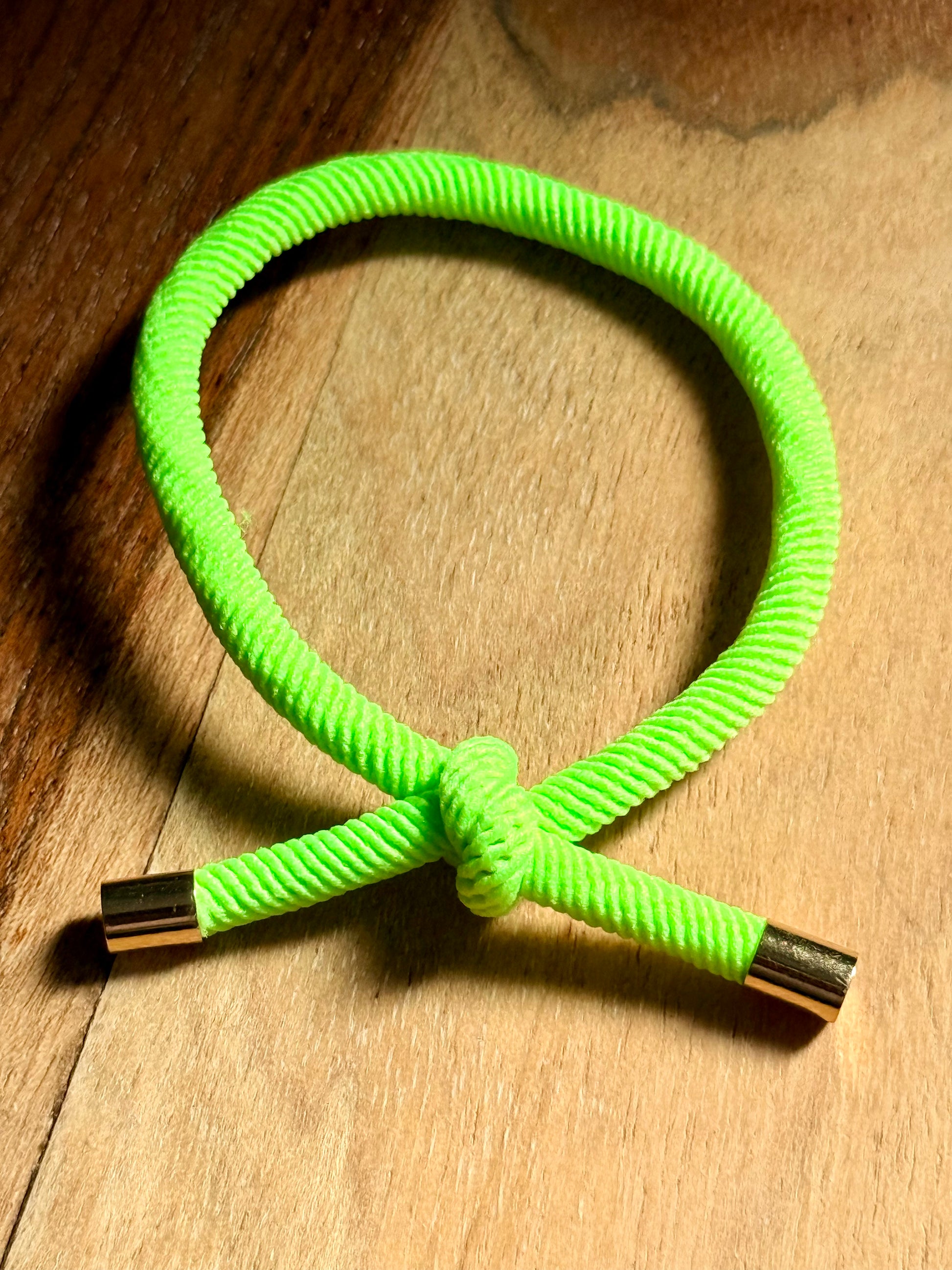 Neon green braided cord with gold ends on a wooden surface