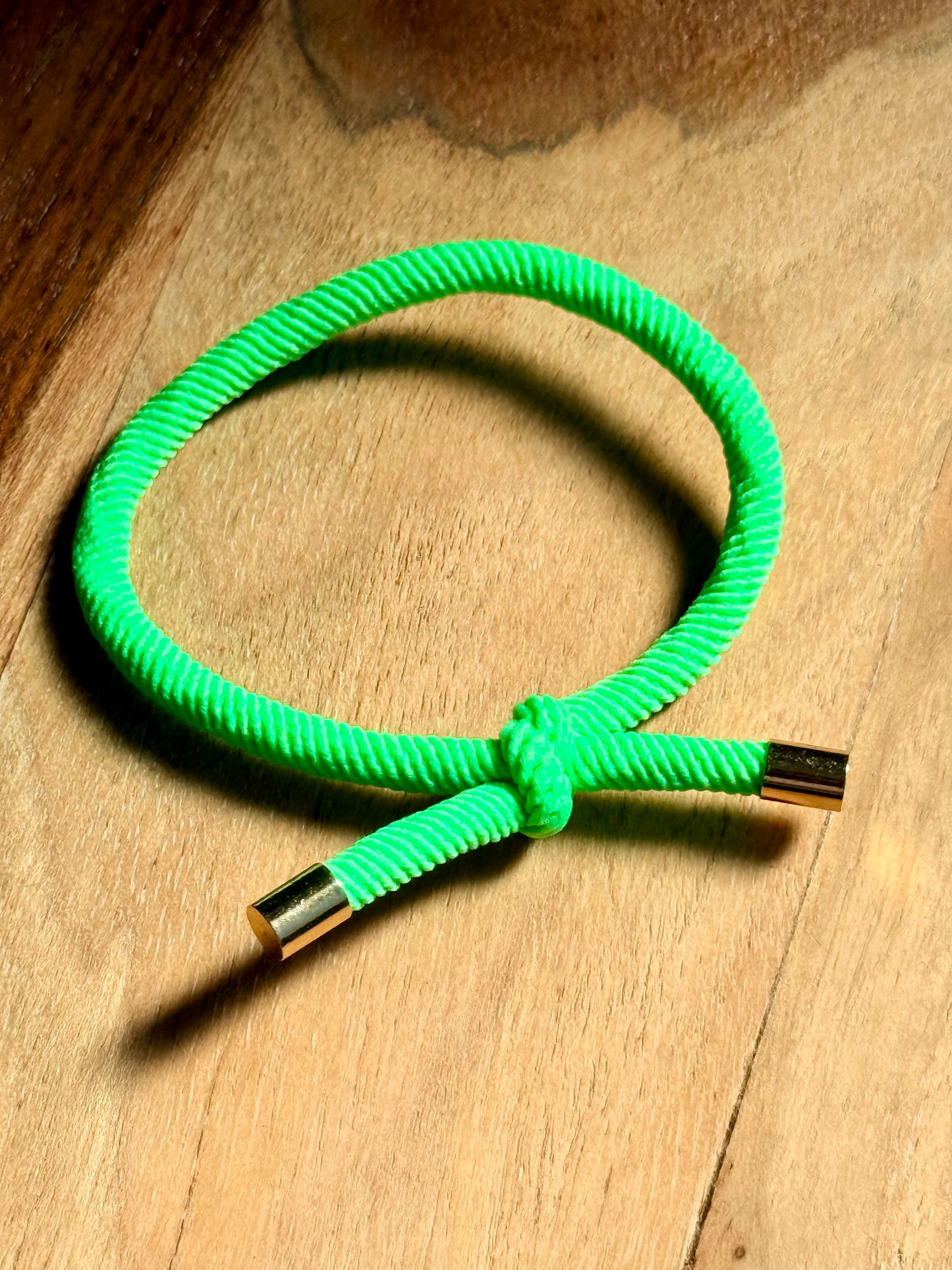 Green braided bracelet with gold clasp on a wooden surface