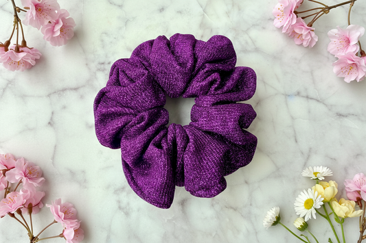 Purple scrunchie on a marble surface with flowers around
