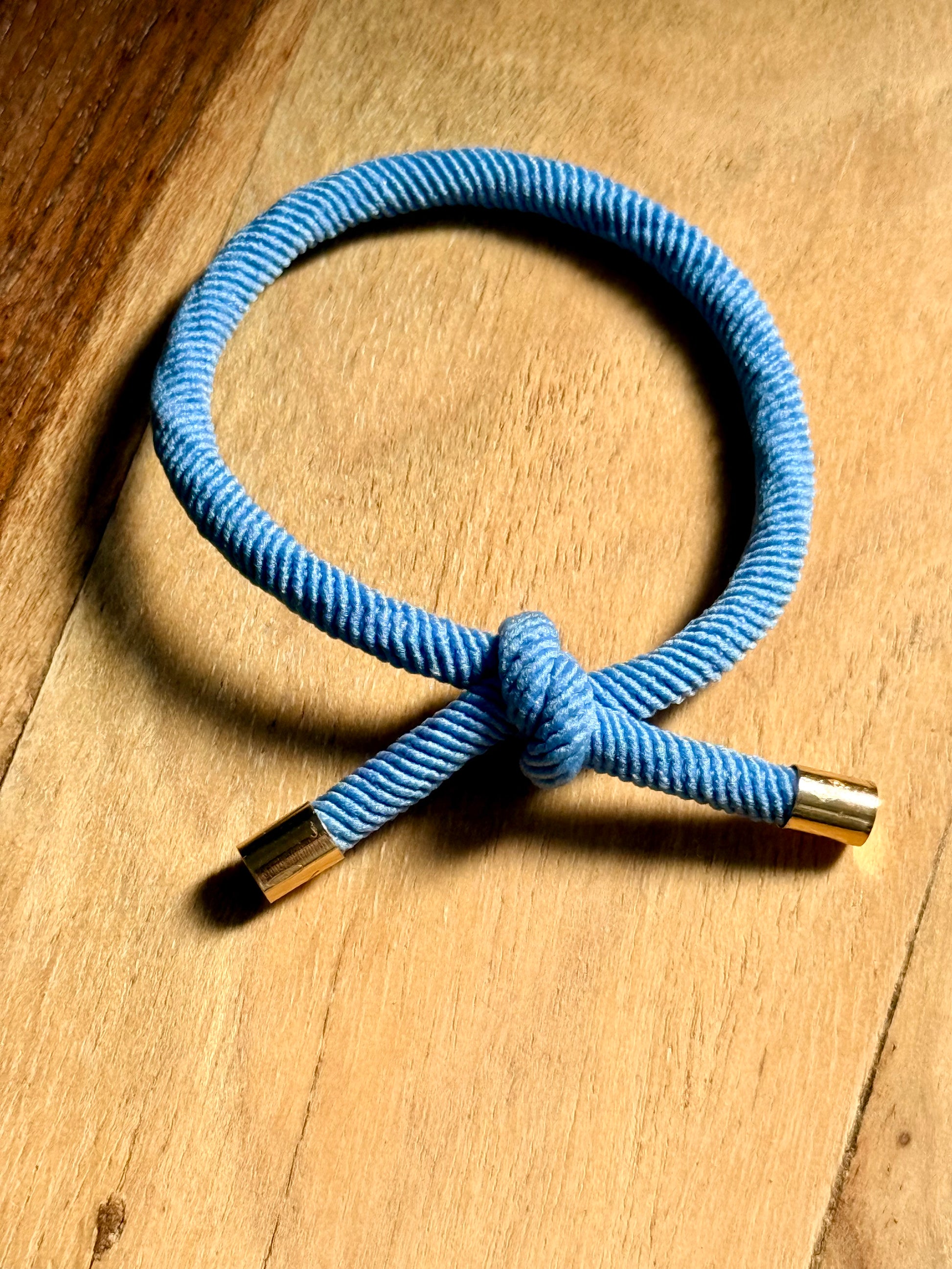 Blue cord bracelet with gold ends on a wooden surface
