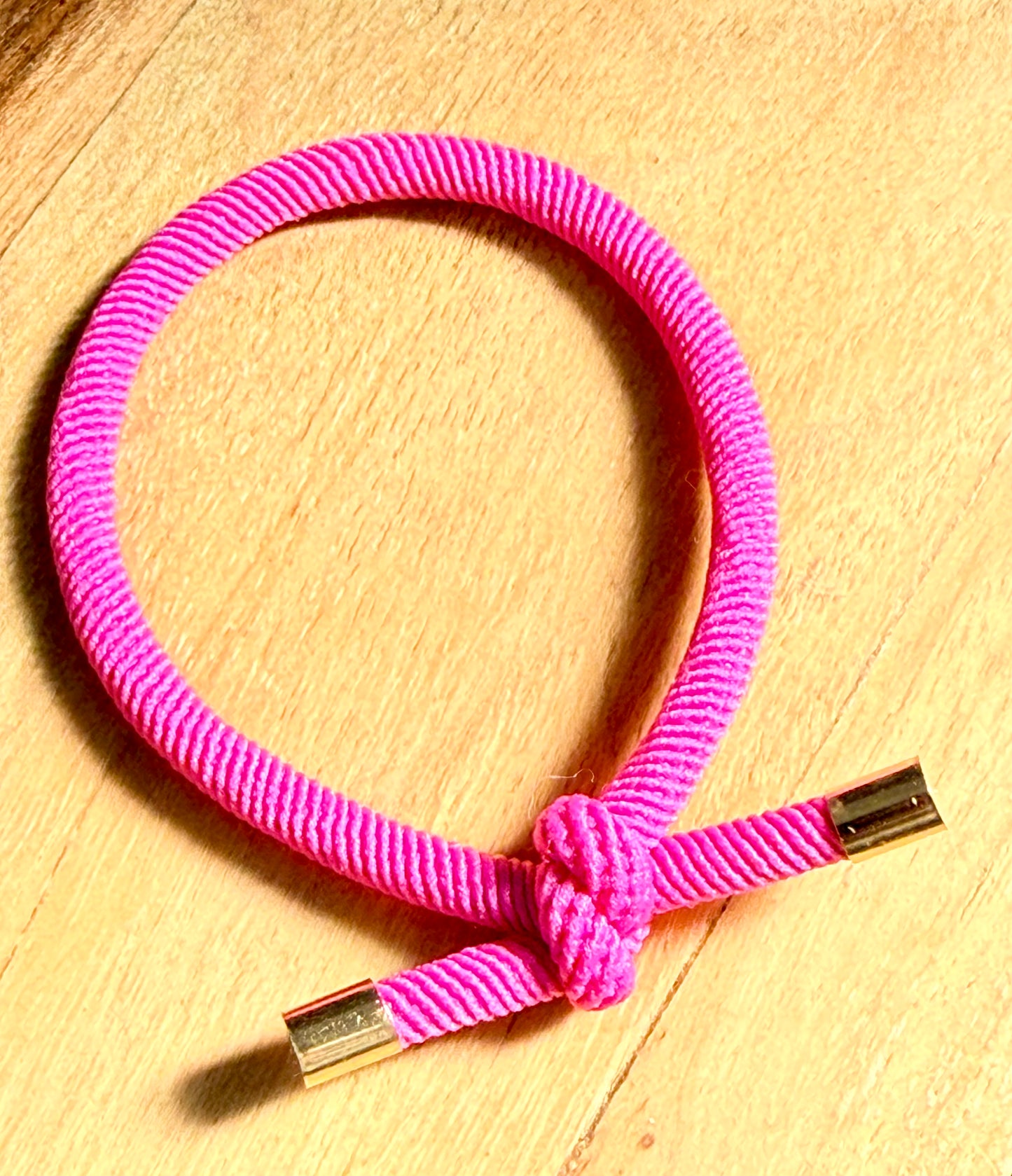 Pink braided bracelet with gold clasp on a wooden surface