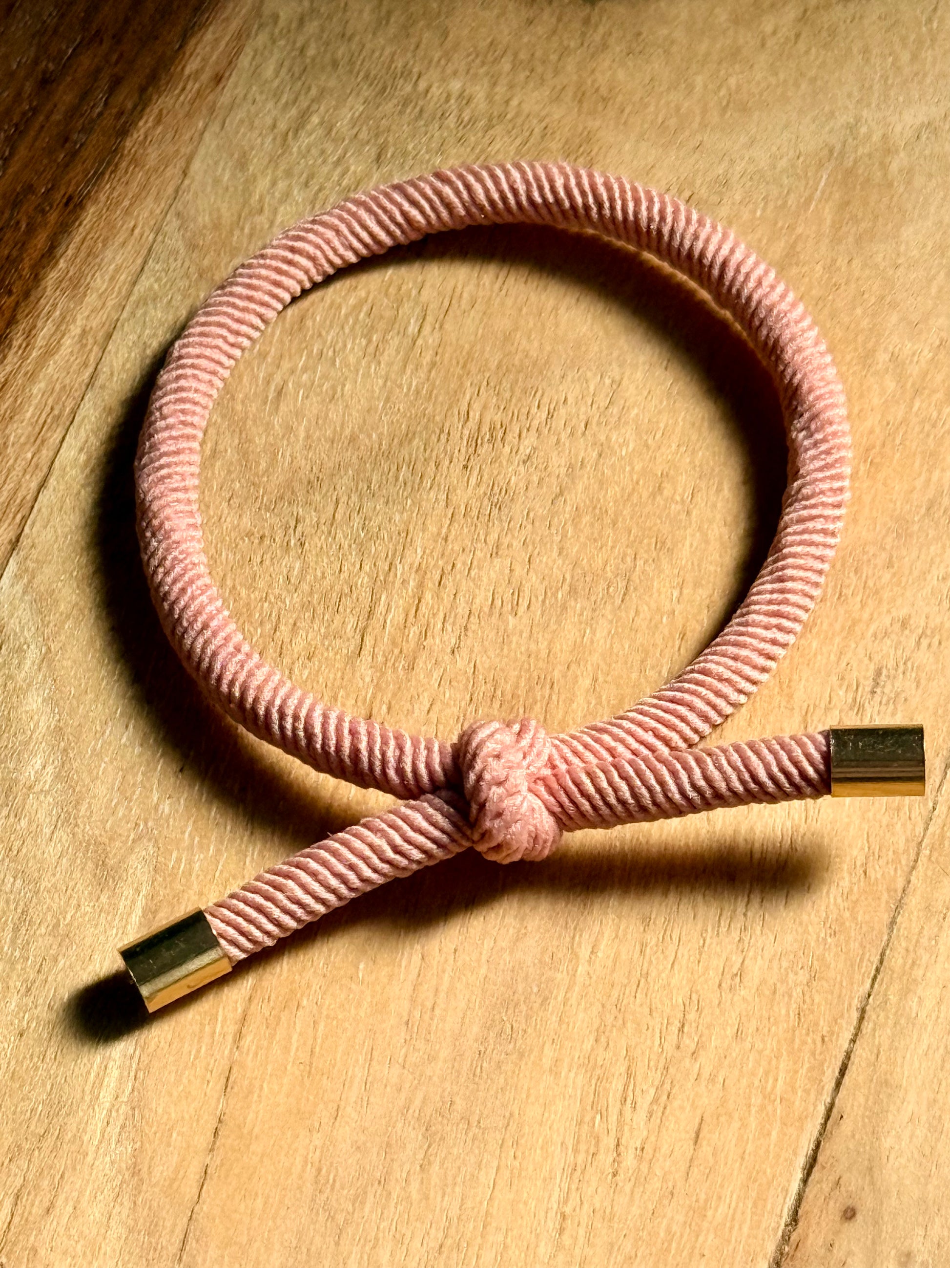 Pink cord bracelet with gold ends on a wooden surface