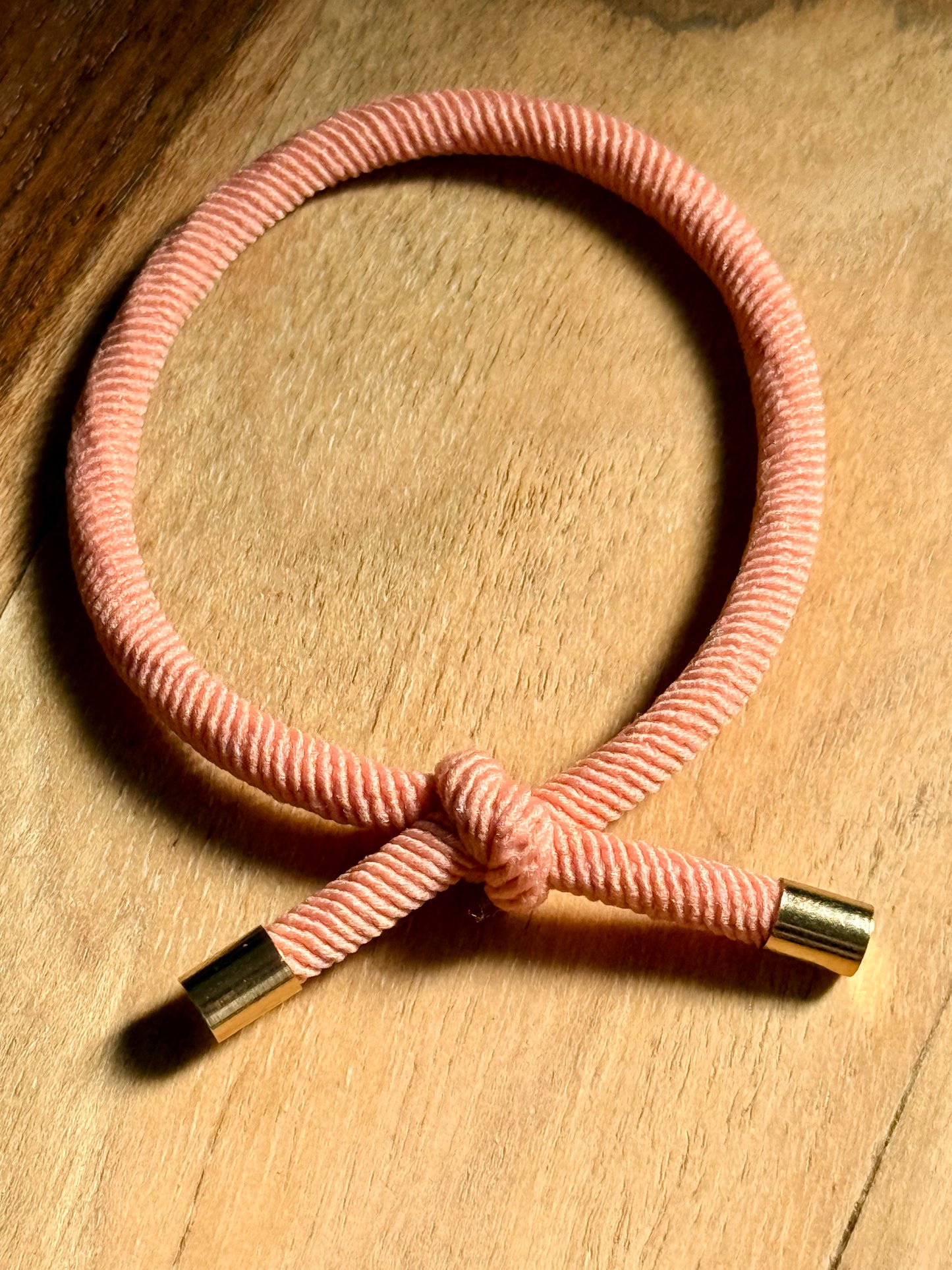 Pink corded bracelet with gold ends on a wooden surface