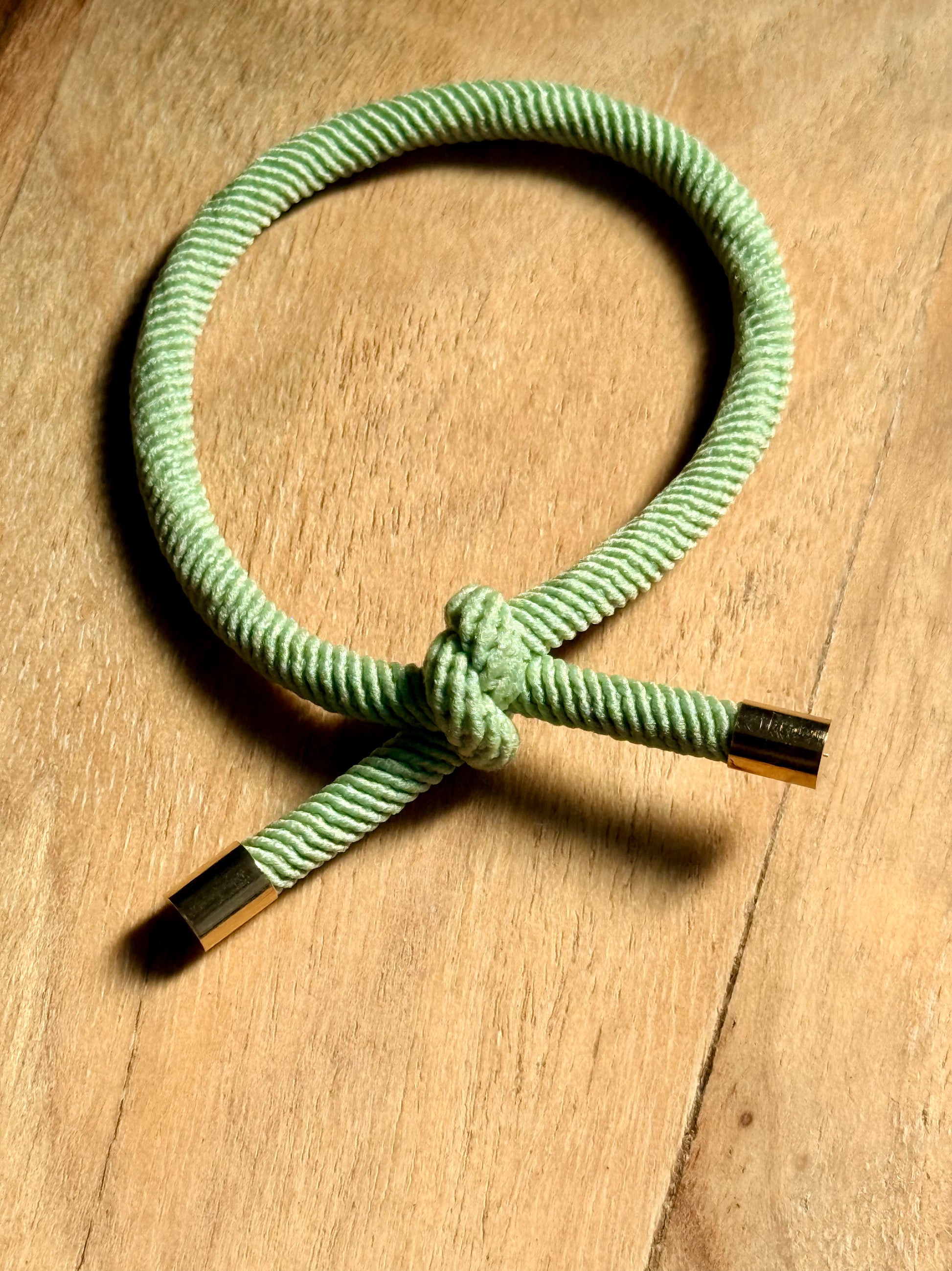 Green rope bracelet with gold ends on a wooden surface