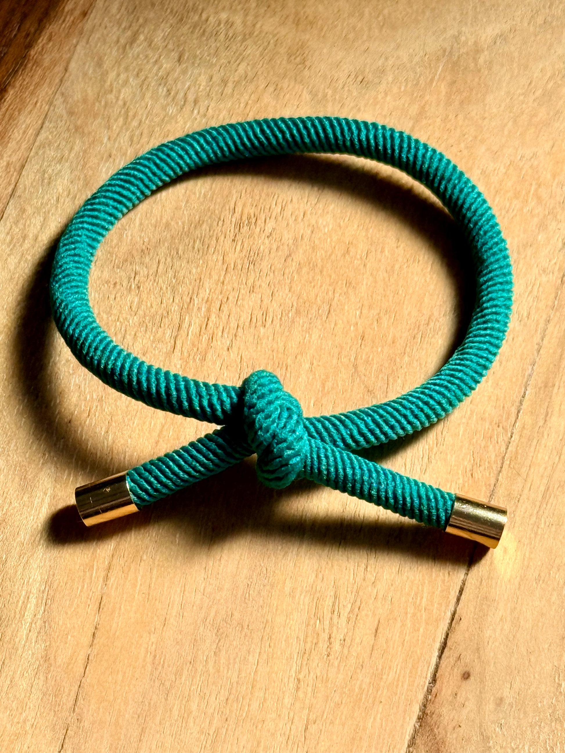 Turquoise cord bracelet with gold clasp on a wooden surface