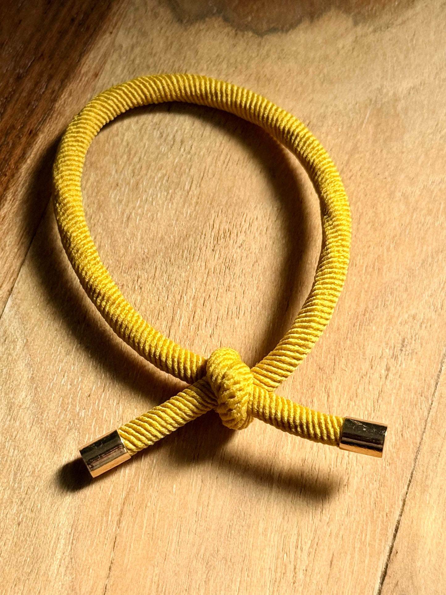 Yellow braided bracelet with metal clasps on a wooden surface